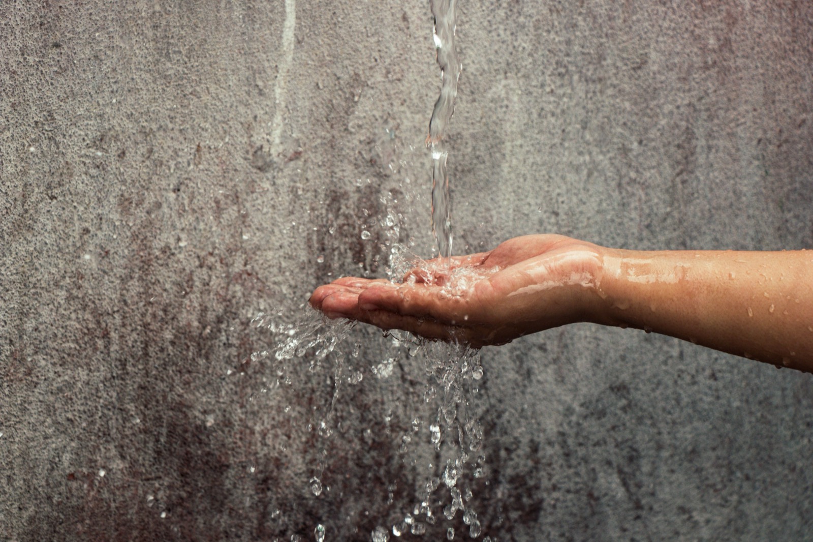 Wasserstrahl trifft auf eine Hand, Sinnbild für Trinkwasser aus der Leitung, Legionellen im Trinkwasser